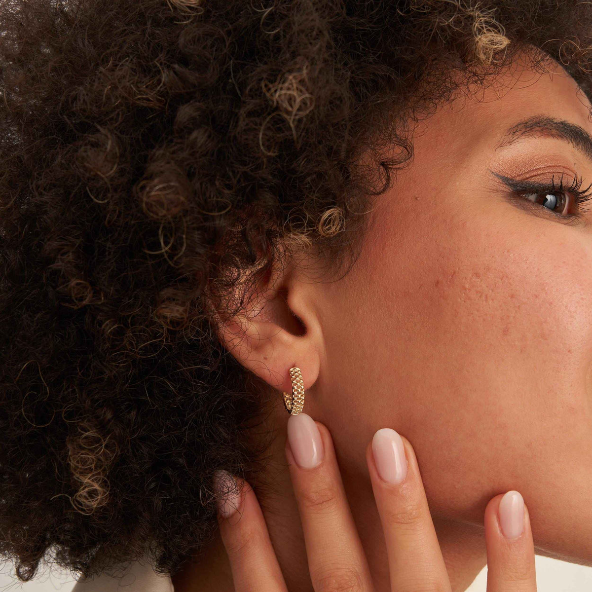 Gros plan sur une oreille avec une créole pointillée en or jaune 14 carats portée, doigts à la mâchoire