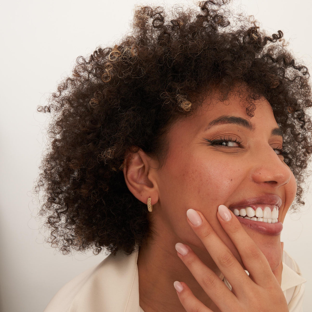 Créoles pointillées en or jaune 14 carats portées par un mannequin souriant, la main sur la joue