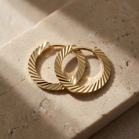 Paire de créoles striées taille diamant en or jaune 14 carats sur une pierre de travertin