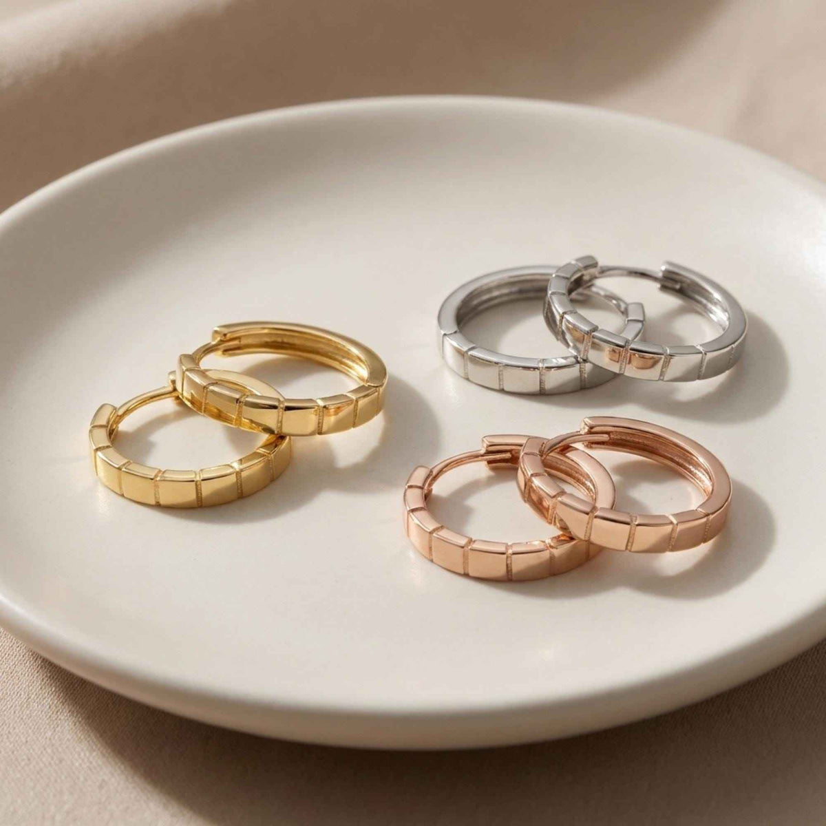 Pendientes de aro segmentados en oro amarillo, blanco y rosa de 14 quilates en un plato de cerámica