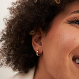 Primer plano de la oreja de la modelo sonriente con un pendiente de aro segmentado en oro amarillo de 14 quilates